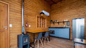 Une cuisine compacte équipée d’un poêle à bois, d’une table à manger avec des chaises et d’un four encastré.