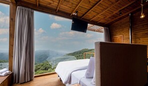 A bedroom with a bed, a wooden ceiling, a large window, and a view of a mountainous landscape. - Linda cabana com jacuzzi VST013 (Anitapolis)