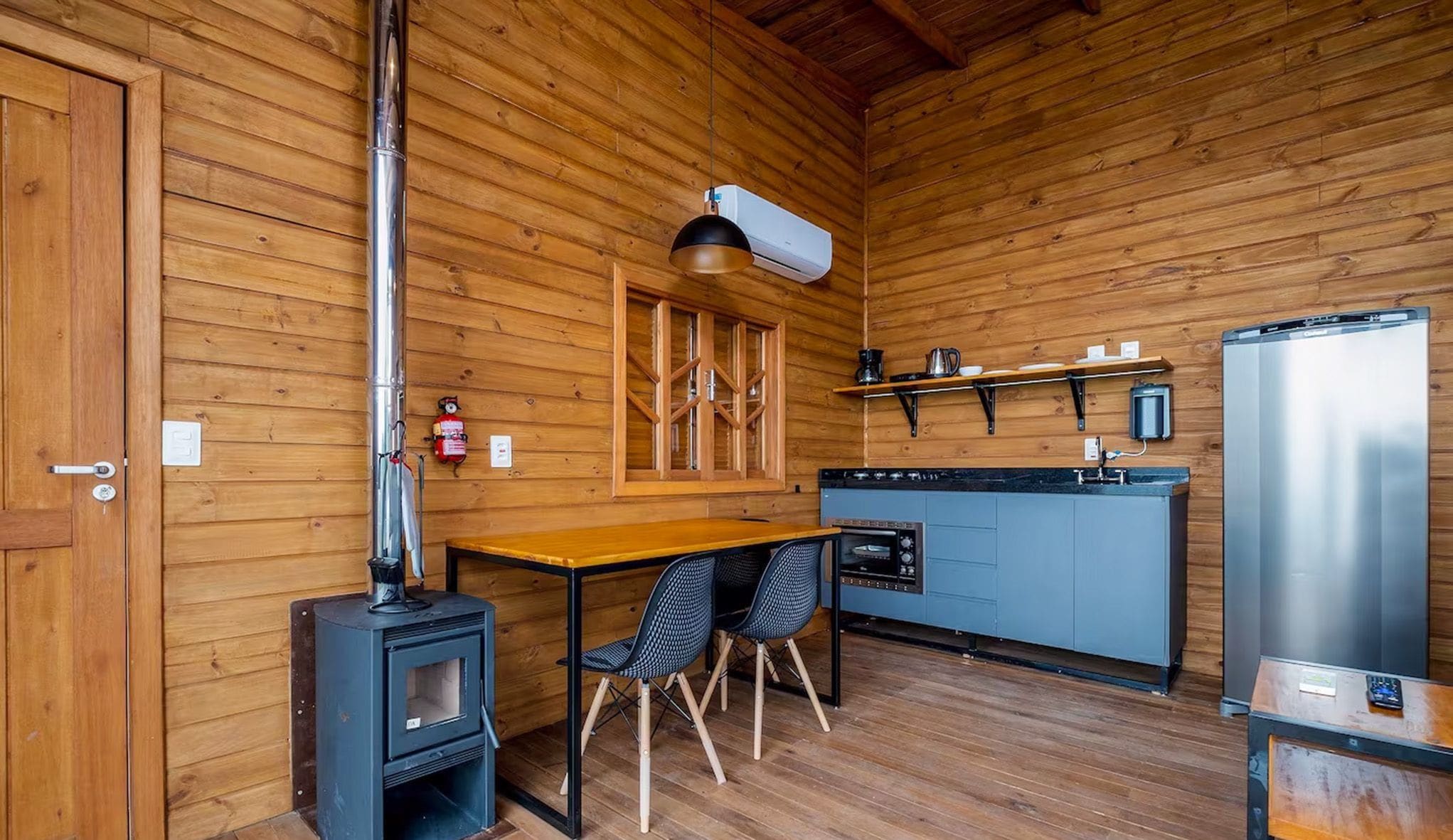 Un interior de madera con cocina, una mesa con sillas, una estufa y un refrigerador.