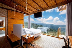 A bedroom with a large window, wooden ceiling, and a bed with white linens.