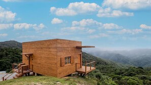 A wooden cabin with a balcony, surrounded by a mountainous landscape.