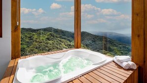 Une terrasse en bois avec un jacuzzi et des serviettes, offrant une vue sur un paysage luxuriant et boisé.