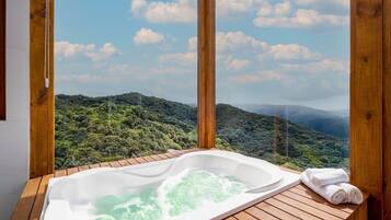 Una terraza de madera con un jacuzzi y toallas, con vistas a un paisaje boscoso exuberante.