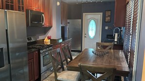 Une cuisine avec des meubles en bois, des appareils électroménagers en acier inoxydable, une table à manger avec des chaises et un tapis à motifs.