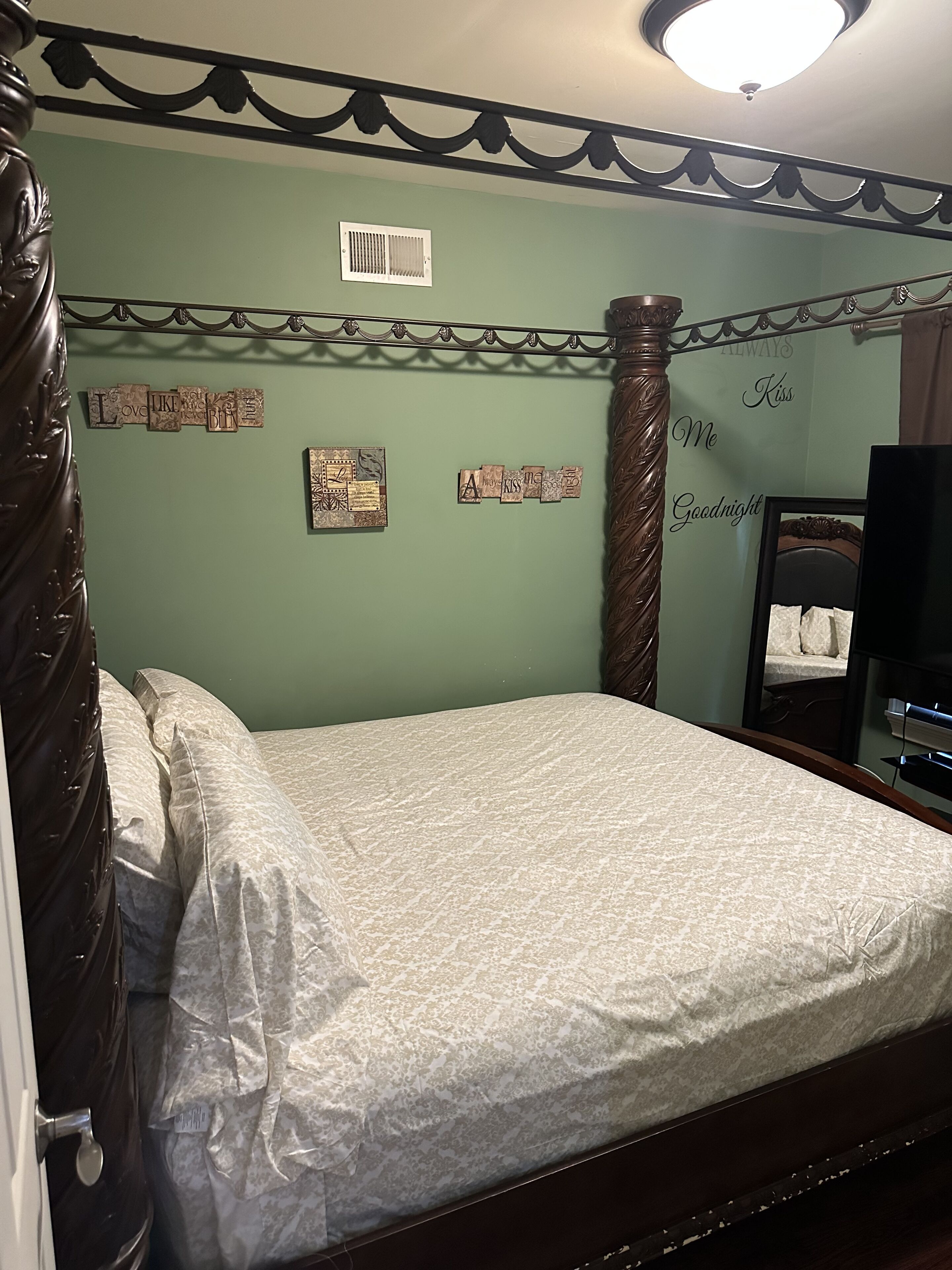 Une chambre à coucher avec un lit, une tête de lit en bois, un mur orné de lettres décoratives, un miroir et un luminaire au plafond.