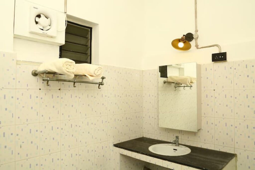 A bathroom with a white tiled wall, a black countertop sink, a towel rack with towels, a mirror, and a wall-mounted light fixture.