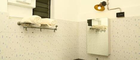 A bathroom with a white tiled wall, a black countertop sink, a towel rack with towels, a mirror, and a wall-mounted light fixture.