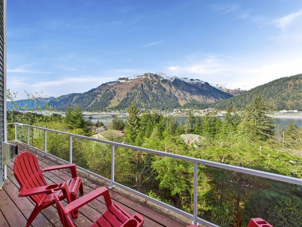 Un balcon avec des fauteuils Adirondack rouges donnant sur un paysage montagneux et un plan d’eau.
