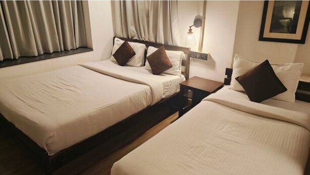 Een hotelkamer met twee bedden, een nachtkastje, een lamp en een raam met gordijnen.
