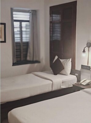 Een hotelkamer met twee enkele bedden, een nachtkastje met lamp, een raam met gordijnen en een deur.