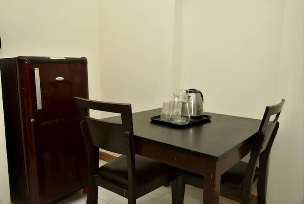 A dining table with chairs, a refrigerator, and a tray with glasses and a kettle.
