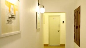 Un pasillo estrecho con suelo de madera, una puerta blanca al final e iluminación en las paredes.