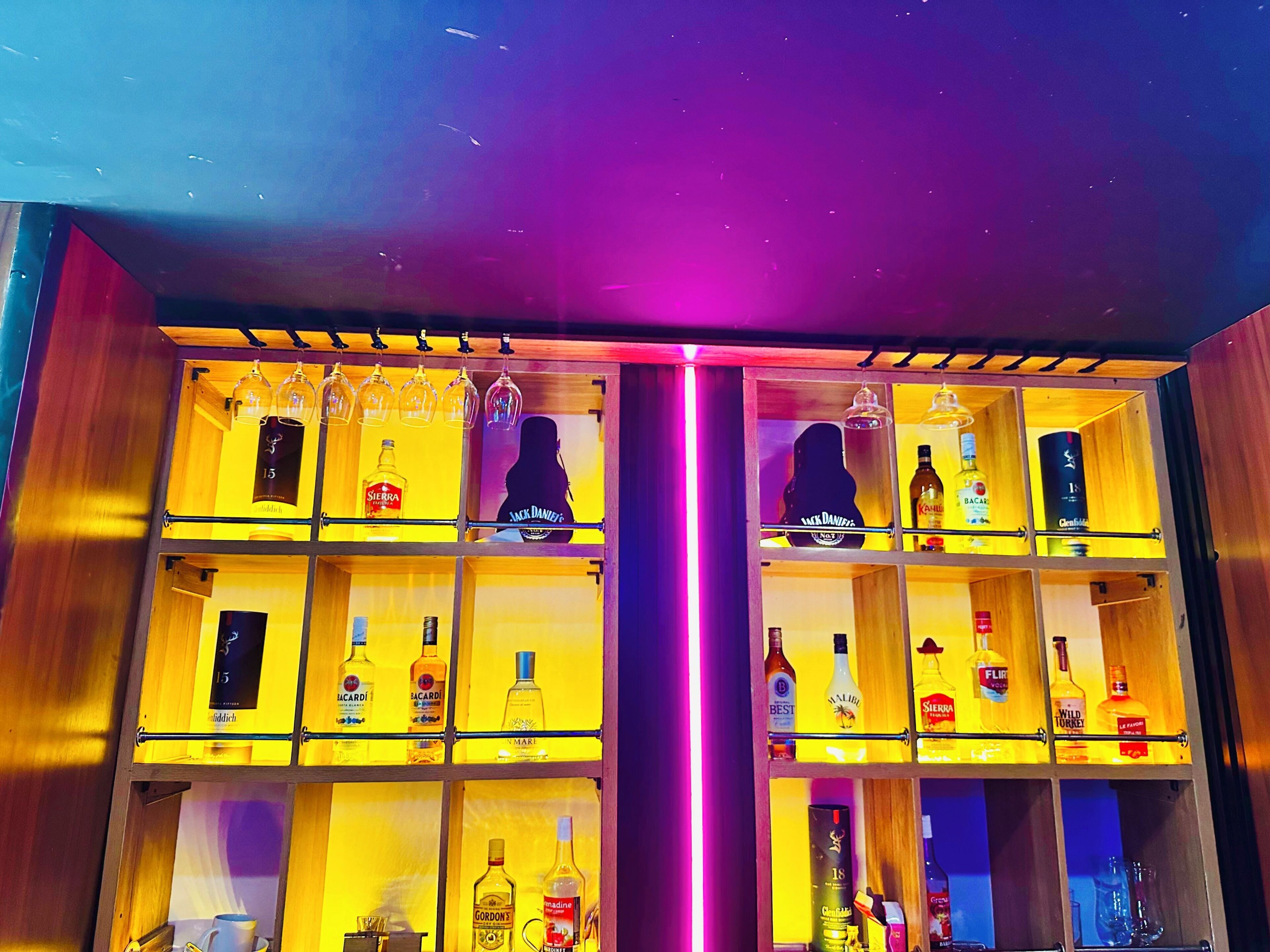 Um balcão de bar com várias prateleiras cheias de garrafas de bebidas e copos.
