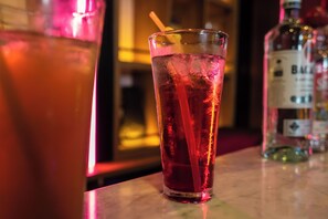 A glass of red beverage with a straw, placed on a bar counter with a bottle of liquor in the background. - Presken Awolowo Way - Ikeja (Lagos)