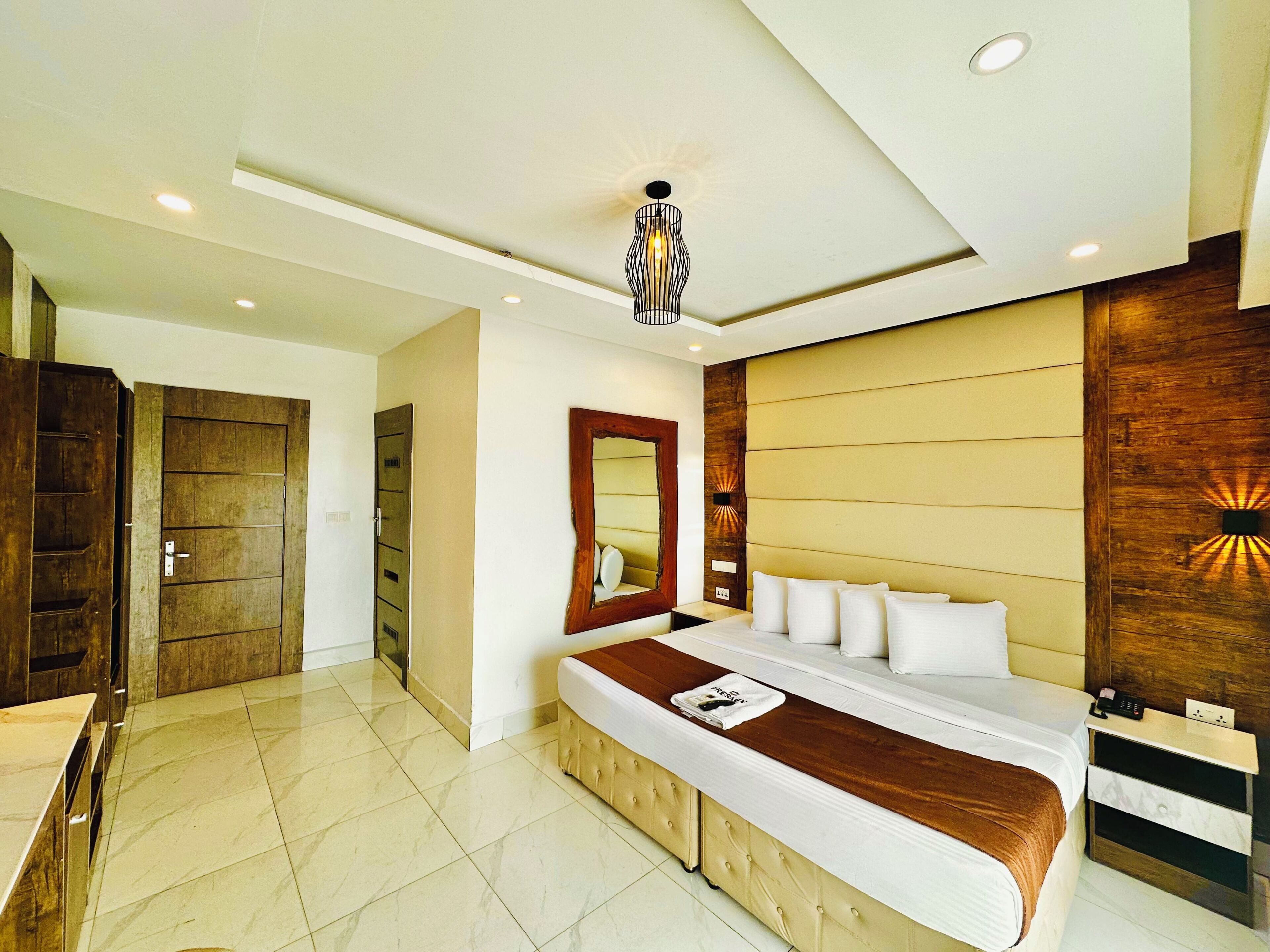 Un dormitorio moderno con una cama grande, un armario de madera, un espejo y una lámpara en el techo.