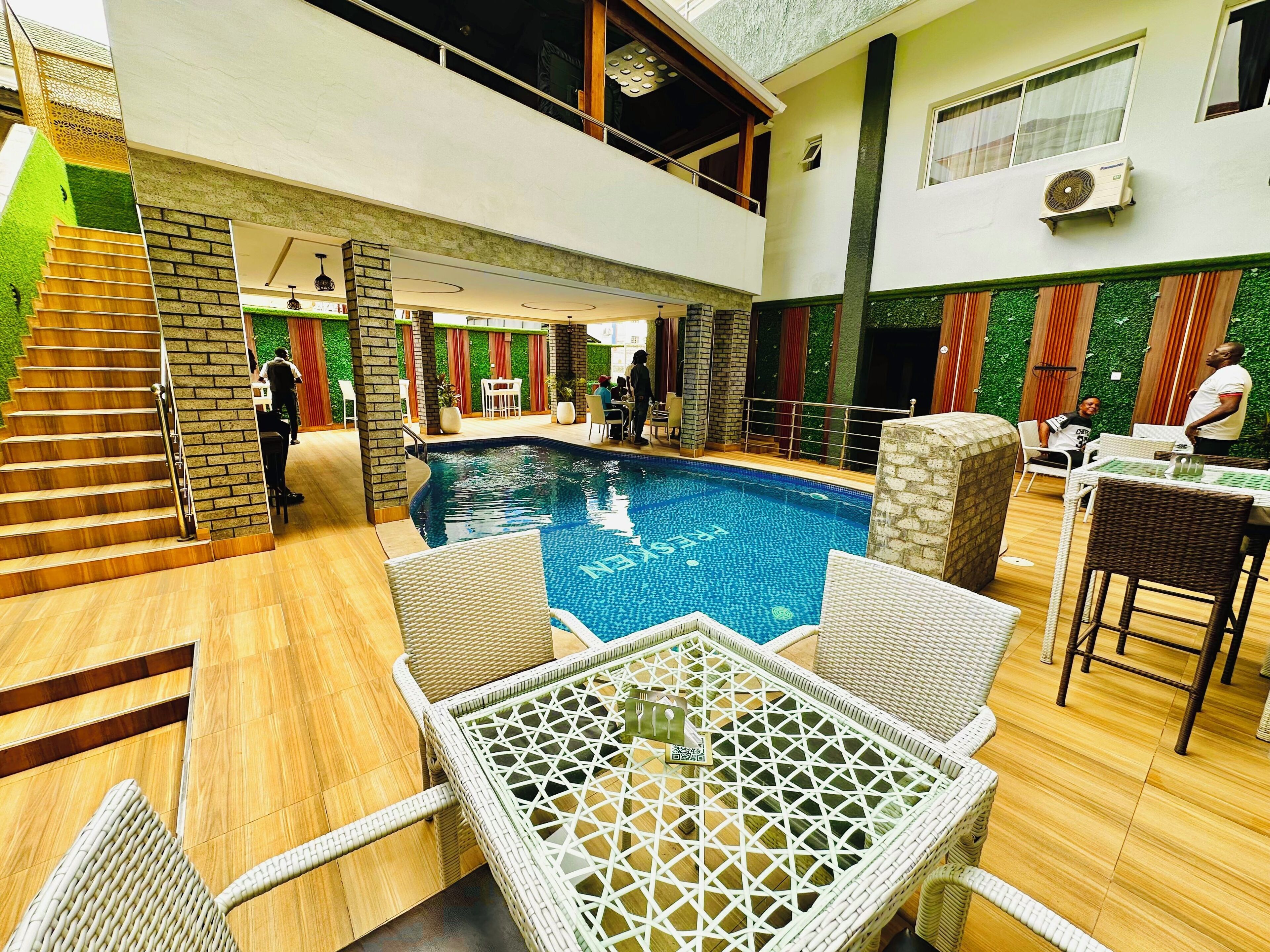 An indoor swimming pool with a view of the upper floor, surrounded by wicker furniture and a staircase.