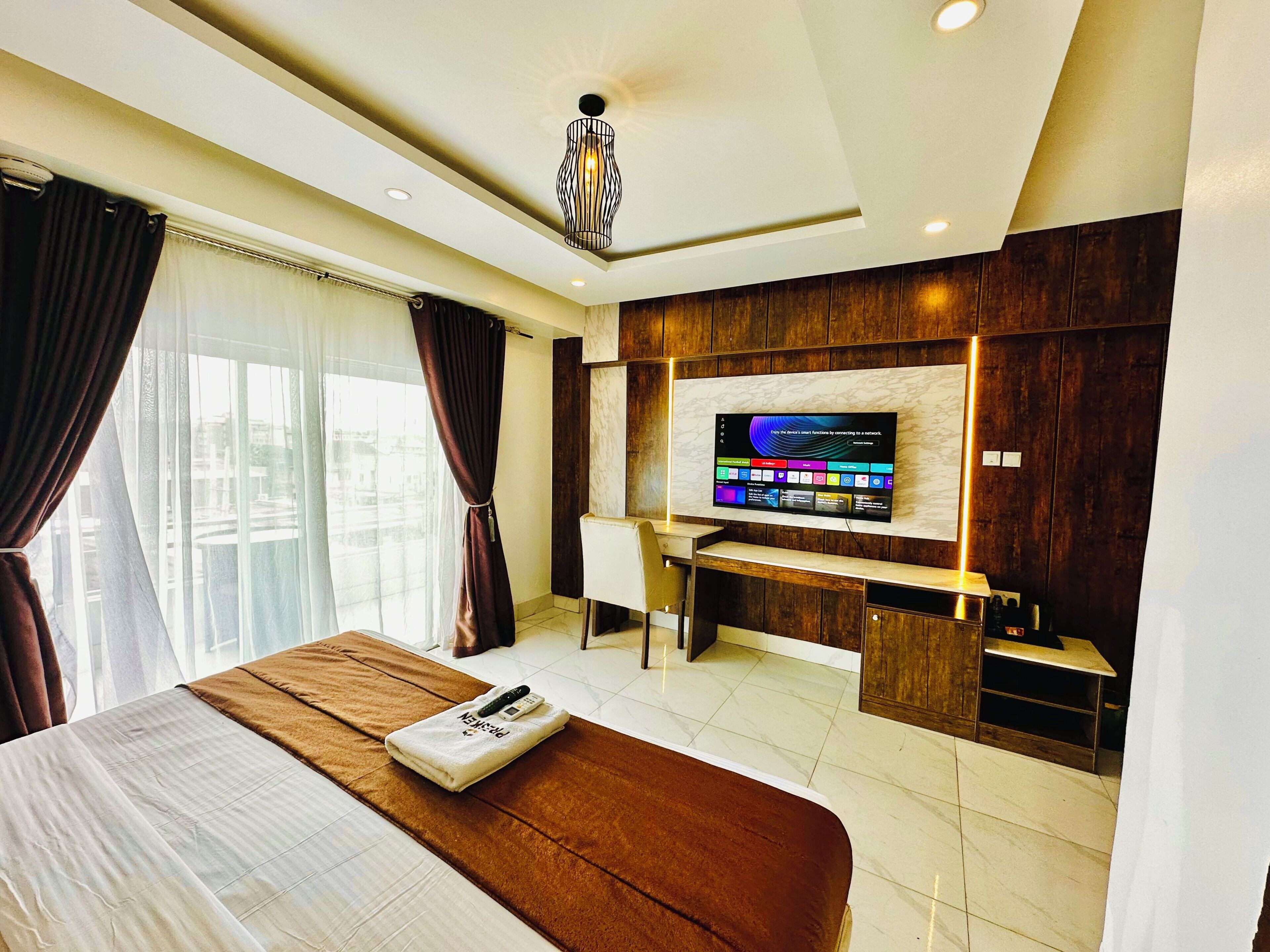 A hotel room with a bed, a desk, a television, and a view of the outside.