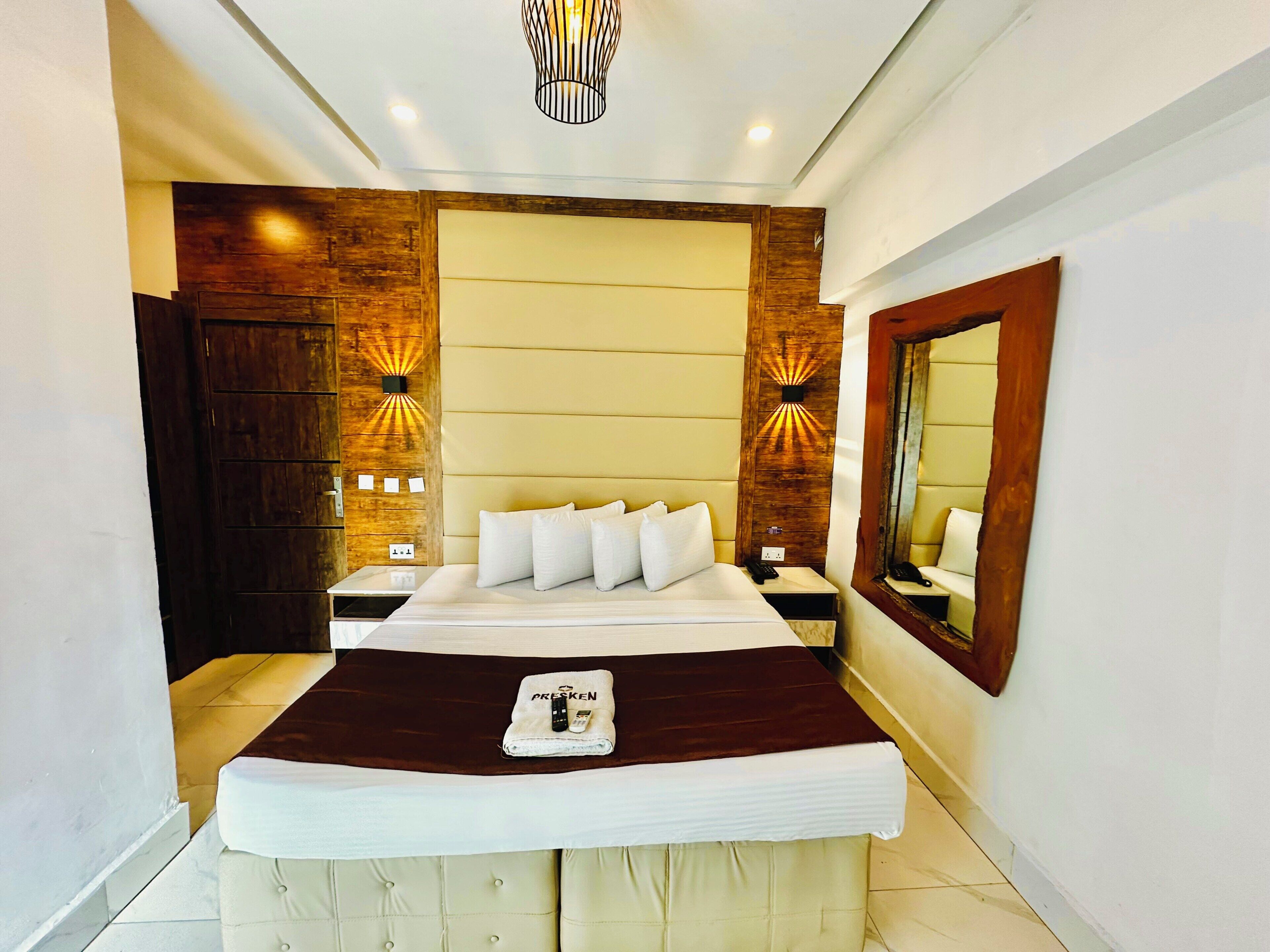 A hotel room with a large bed, bedside tables, a mirror, and wall-mounted lighting.