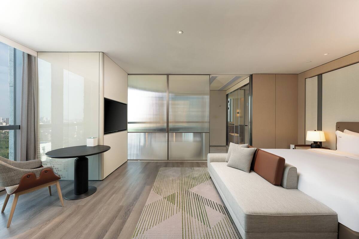 Une chambre d’hôtel moderne, équipée d’un canapé, d’une petite table, d’une télévision et d’une grande fenêtre.