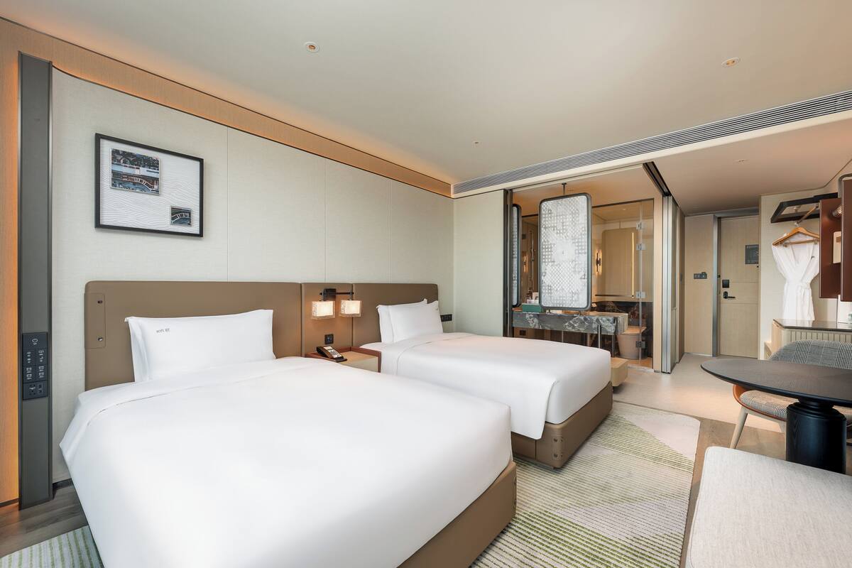 Une chambre d’hôtel avec deux lits, un bureau, une chaise, un miroir et un tableau encadré au mur.