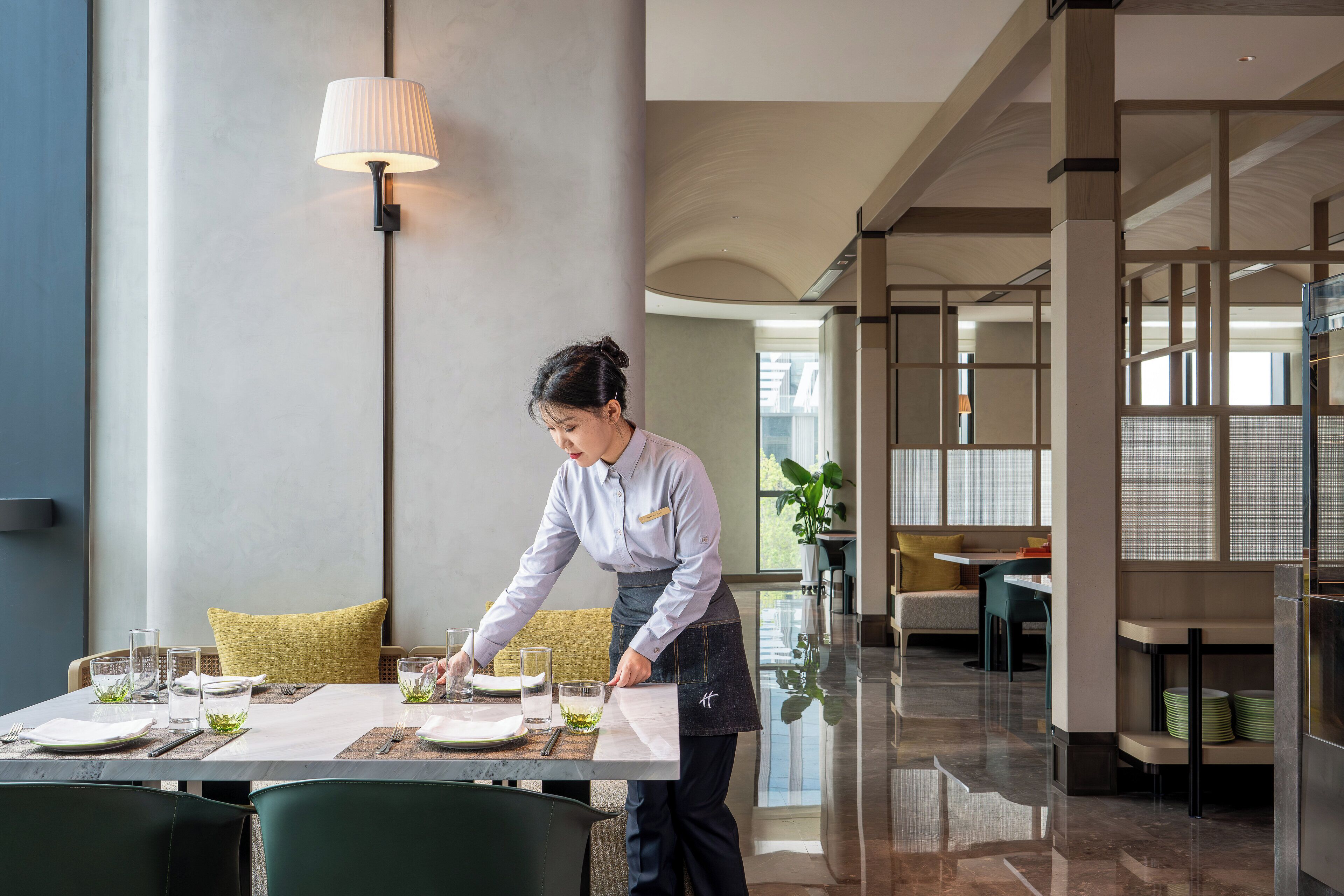 Un comedor moderno con un diseño limpio y minimalista, que destaca un piso de mármol pulido, una mesa bien iluminada con mantel blanco y una lámpara contemporánea.