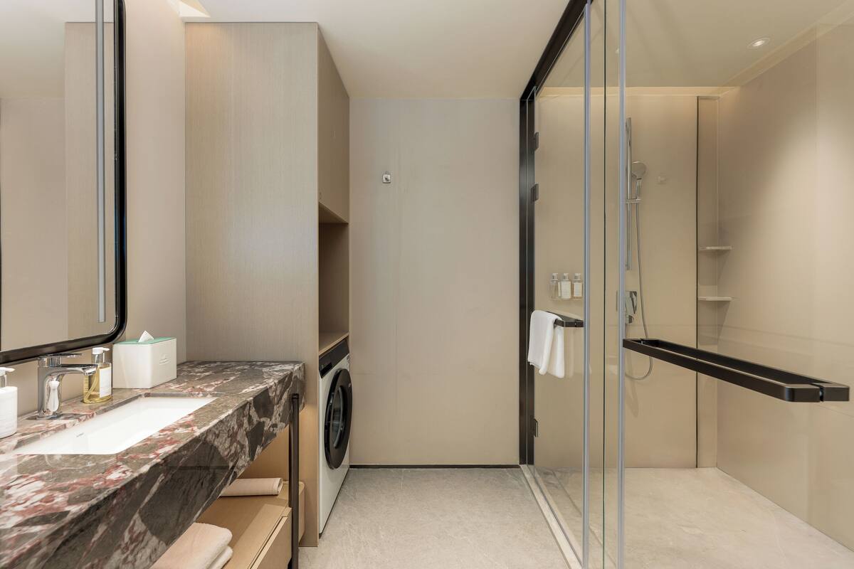 Une salle de bain moderne avec un lavabo en marbre, un lave-linge, une cabine de douche en verre et un grand miroir.