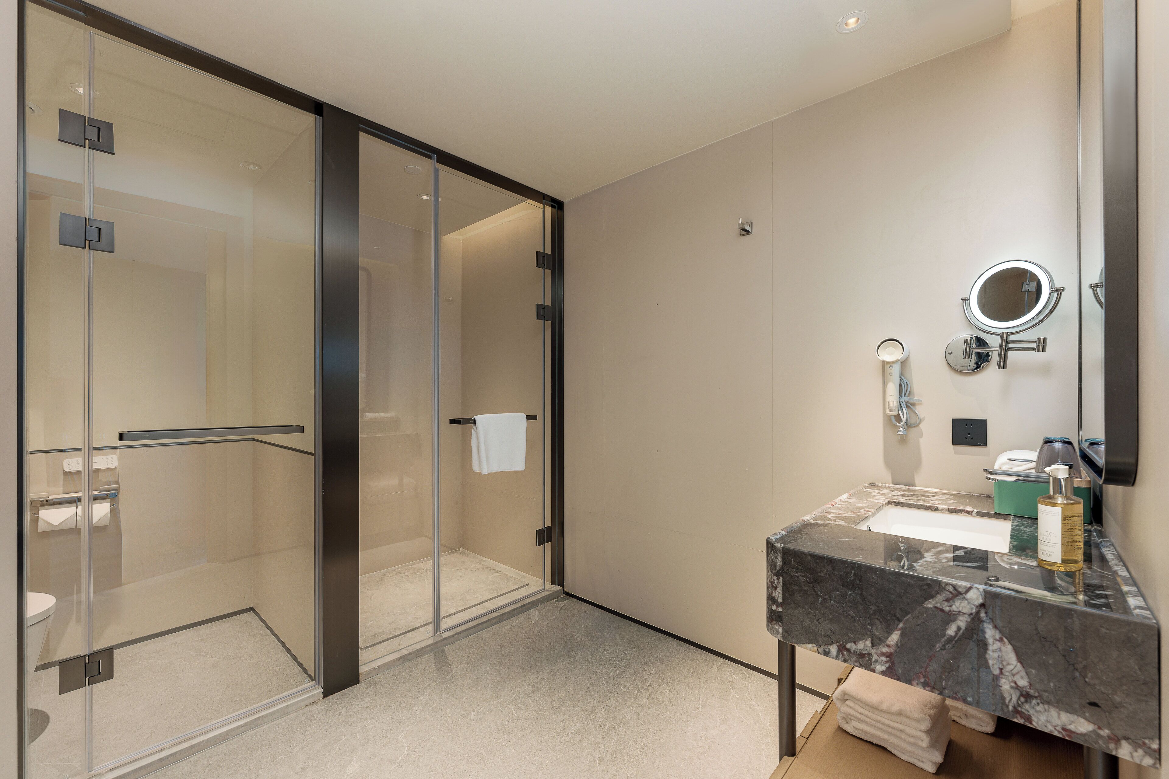 Un baño moderno con ducha envuelta en vidrio, lavamanos de mármol y un espejo grande.