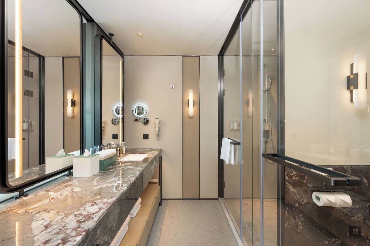 Une salle de bain moderne avec un meuble-lavabo en marbre, une cabine de douche en verre et un grand miroir.
