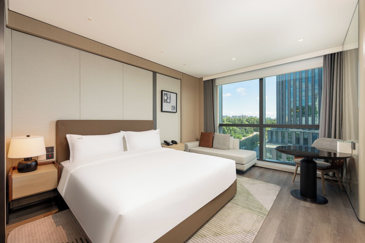 Habitación de hotel moderna con una cama grande, un escritorio y vistas a la ciudad.