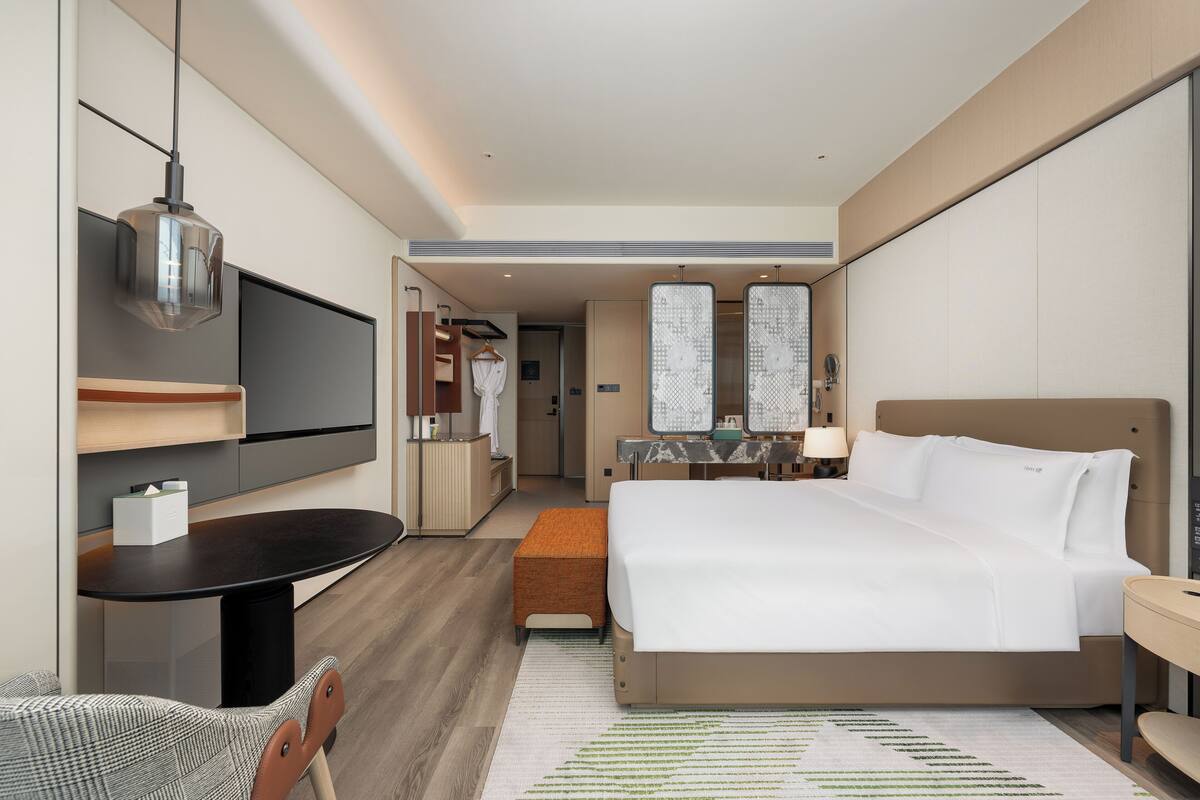 Une chambre d’hôtel moderne dotée d’un grand lit, d’un bureau avec une chaise, d’une télévision et d’un dressing.