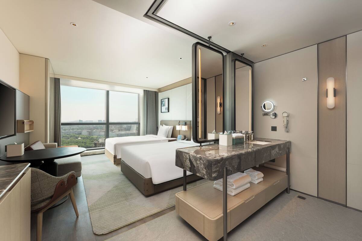 Une chambre d’hôtel dotée d’un grand lit, d’un bureau, d’une salle de bain avec un lavabo et d’une grande fenêtre donnant sur la ville.