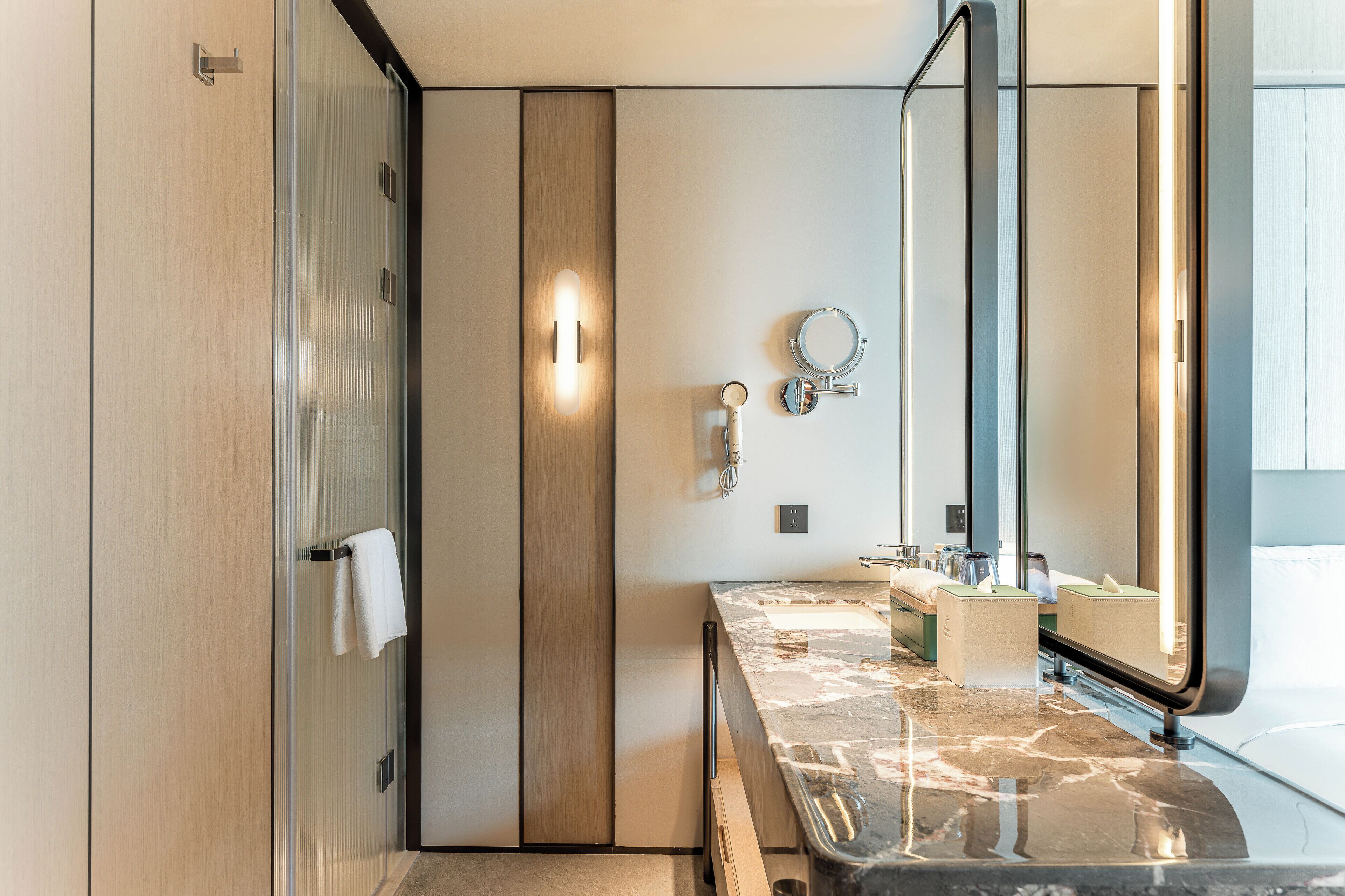A modern bathroom with a glass shower enclosure, a marble countertop, and a large mirror.
