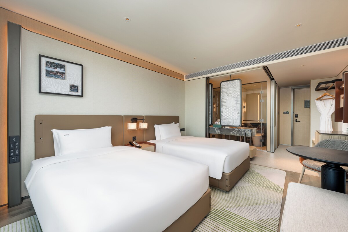 Habitación de hotel con dos camas, un escritorio, una silla, un espejo y un cuadro en la pared.
