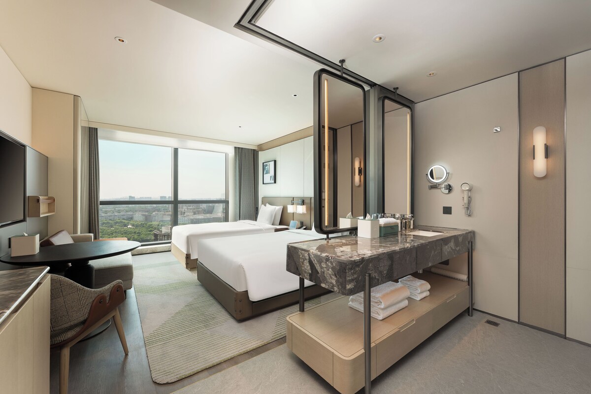 Habitación de hotel con una cama grande, un escritorio, un baño con tocador y un ventanal con vistas a la ciudad.