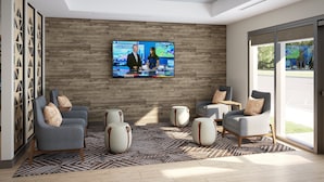 Moderni aula, jossa on suuri televisio, jolta näkyy uutisia, mukavat istuimet ja näkymä ulos.