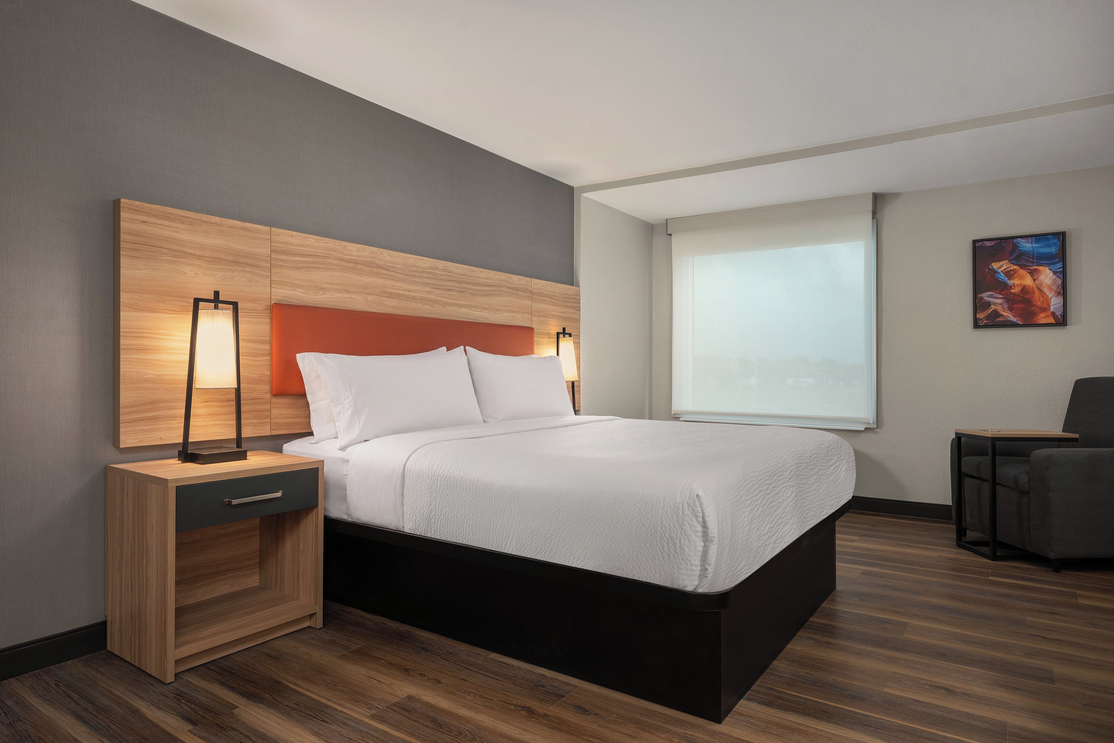 A modern hotel room with a bed, bedside tables, a desk, and a window.