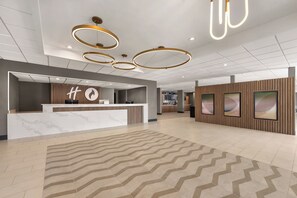 A modern hotel lobby with a reception desk, a large clock, and a dining area in the background. - Candlewood Suites Orlando North Winter Park by IHG (Orlando)