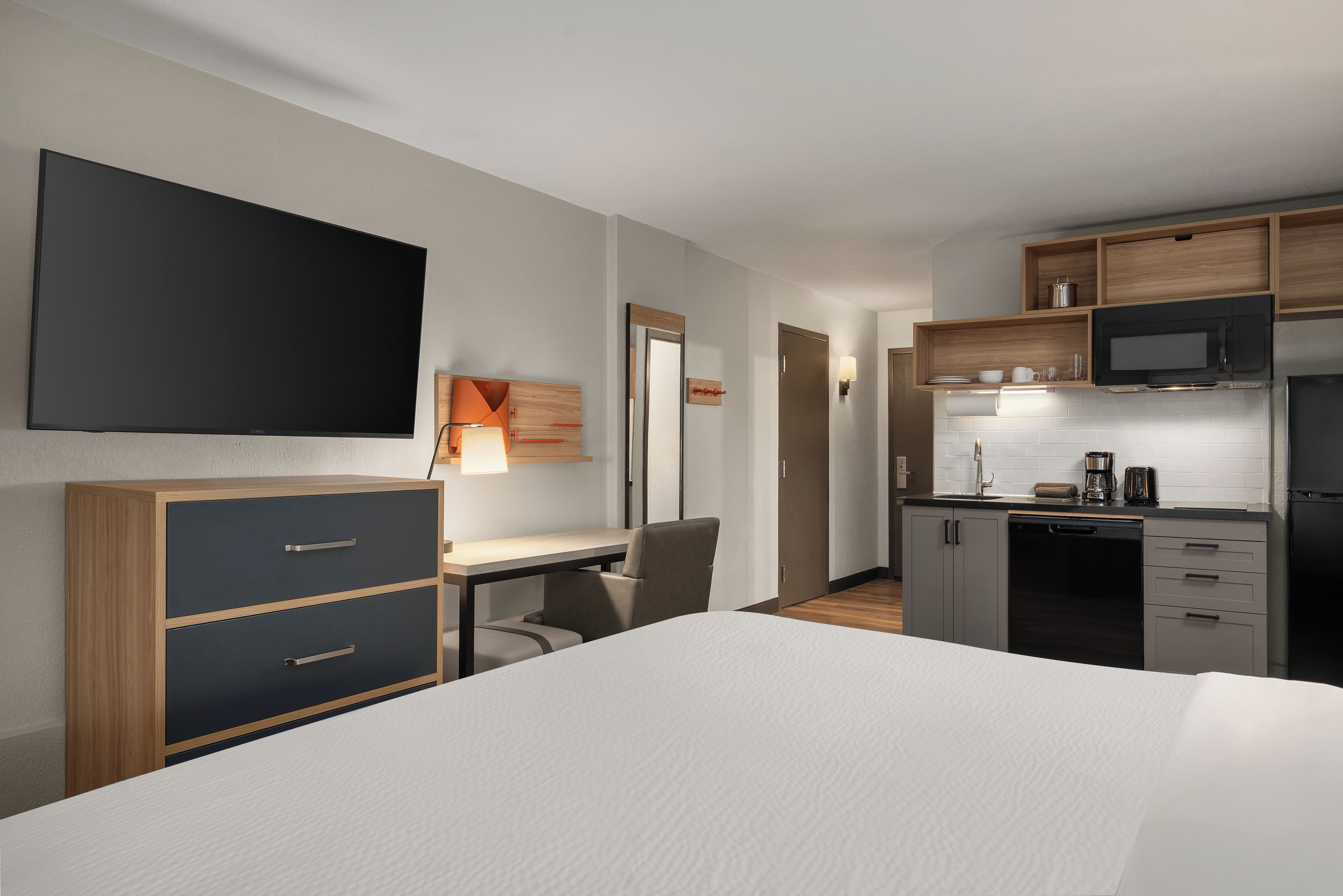 A hotel room with a bed, a desk, a chair, a television, a microwave, and a kitchenette.