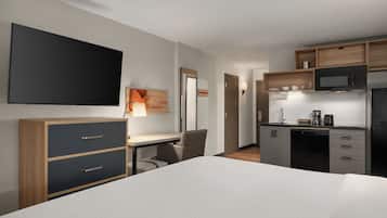 A hotel room with a bed, a desk, a chair, a television, a microwave, and a kitchenette.