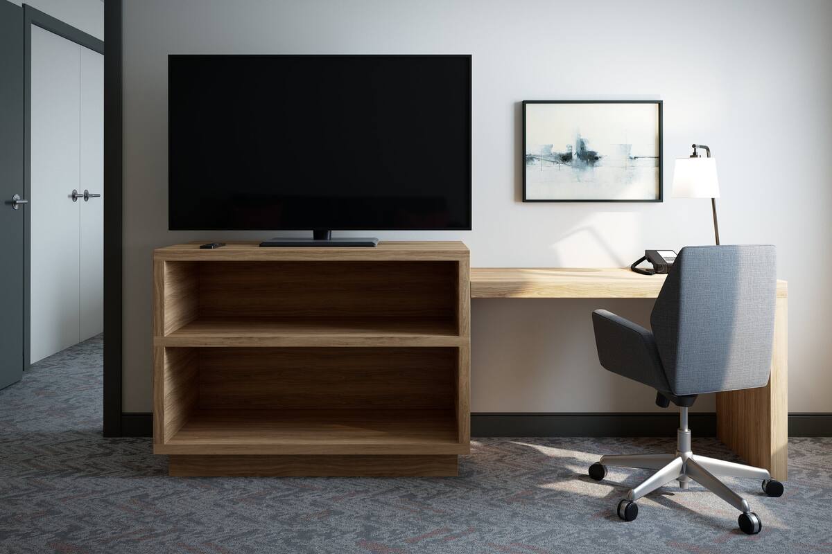 Une chambre d’hôtel avec un téléviseur posé sur un meuble en bois, un bureau avec une chaise et un tableau encadré accroché au mur.