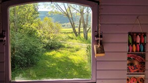 Ett fönster med utsikt över ett grönskande landskap, en trädörr och en hylla med färgglada föremål.