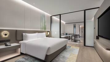 A modern hotel room with a large bed, bedside controls, a flat-screen TV, and a seating area with a table and chairs.