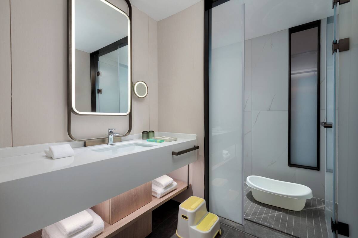 A modern bathroom with a large mirror, a white sink, and a glass-enclosed shower area.