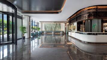 Un moderno hall de hotel con un mostrador de recepción curvo, zona de estar y grandes ventanales que ofrecen vistas al exterior.