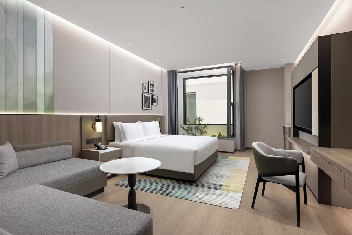 A modern hotel room with a large bed, a sofa, a desk, and a TV.
