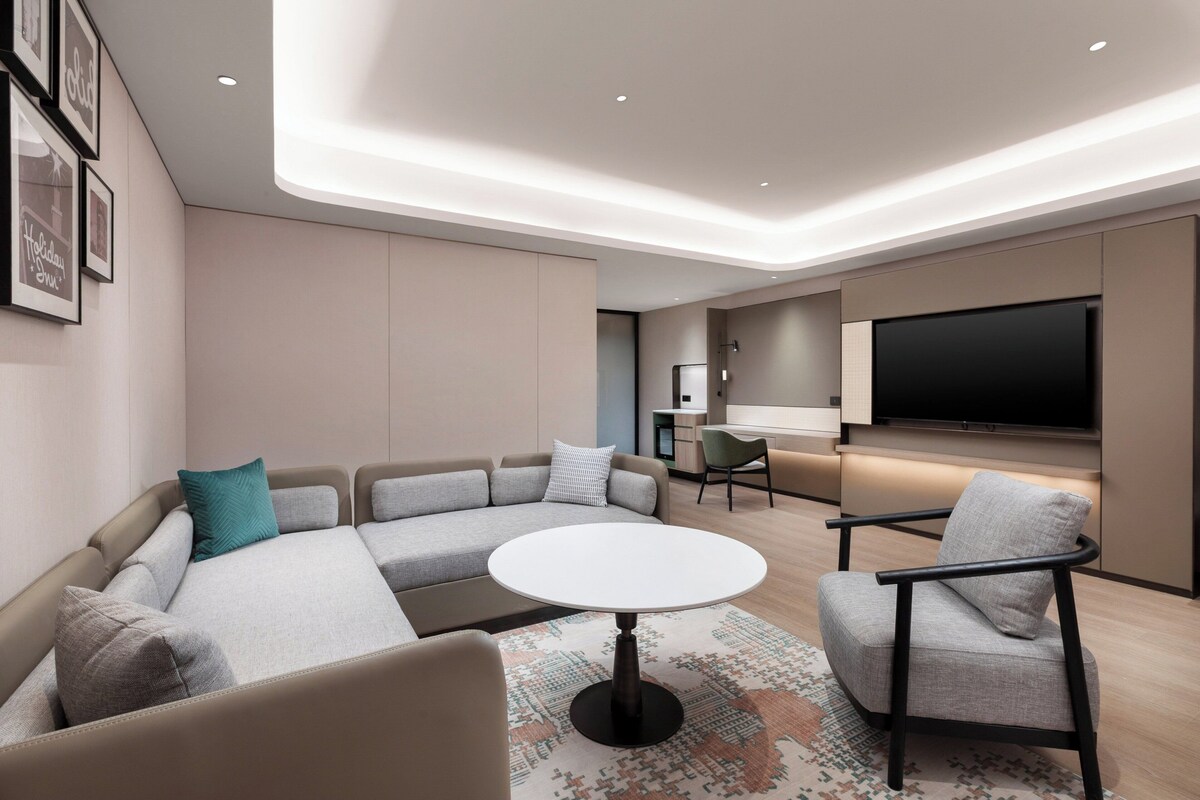 A modern living room with a sectional sofa, a round coffee table, and a flat-screen TV mounted on the wall.