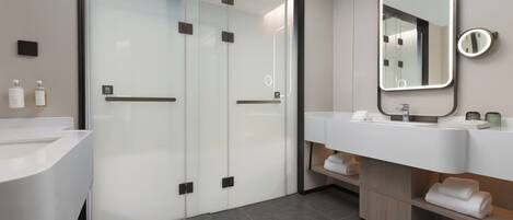 Une salle de bain moderne avec une douche à parois de verre, un grand miroir et un meuble-lavabo doté d’un évier et d’un porte-serviettes.
