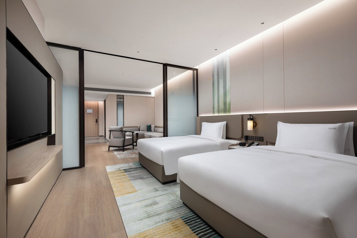 A modern hotel room with two beds, a flat-screen TV, a desk, and a sofa.