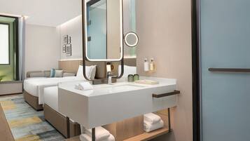 Una habitación de hotel moderna con una cama grande, un sofá independiente, una tocador con espejo y un pequeño rincón de descanso.