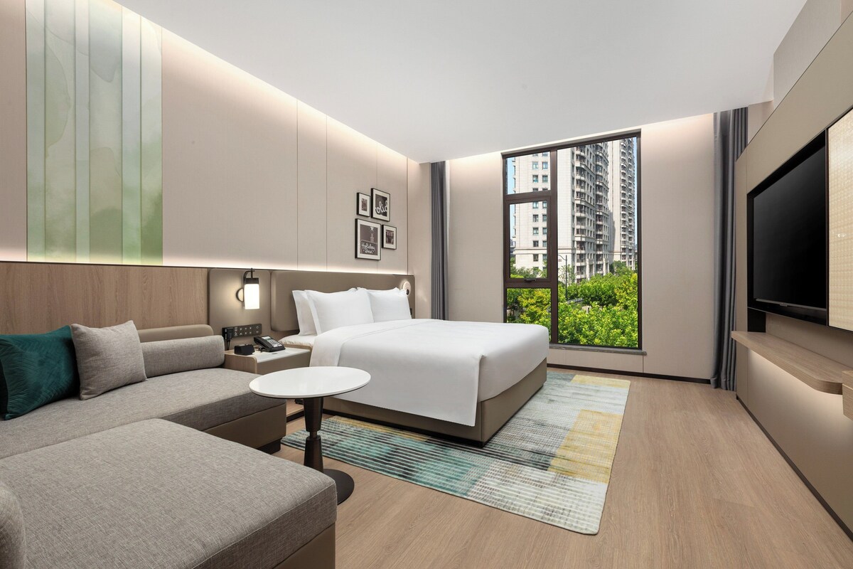 A modern hotel room with a large bed, a sofa, a small table, and a TV.